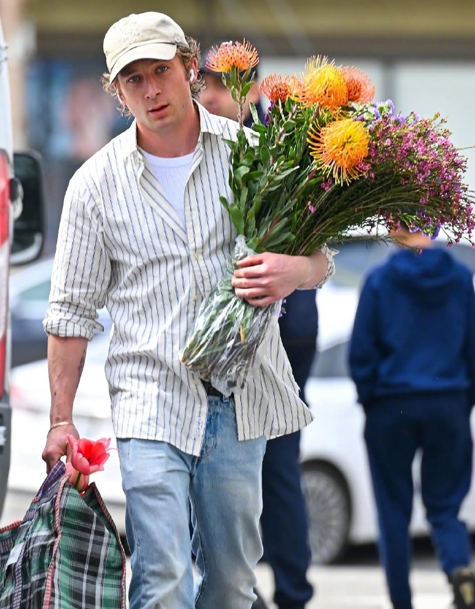 A man in a striped shirt holding flowers — Jeremy Allen White.