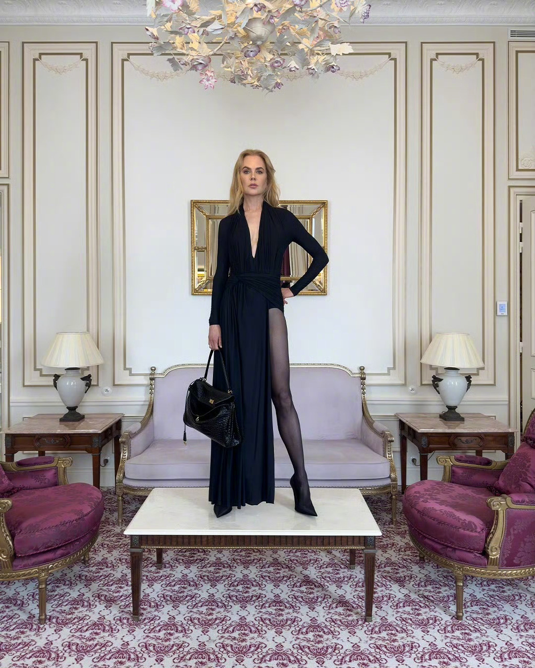 Nicole Kidman stands on a table wearing black stockings and black high heels.
