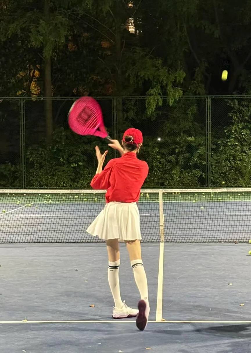 Girl playing tennis, in bright red top and white pleated skirt and knee-high socks