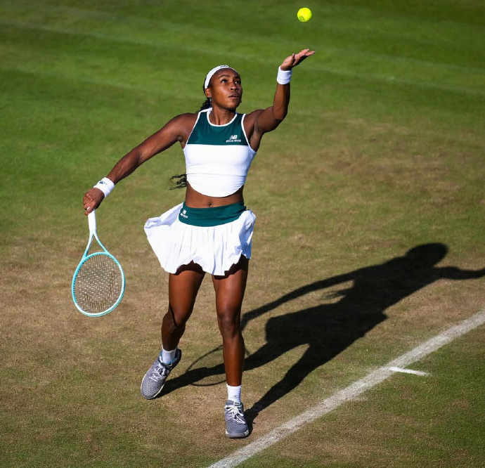 Coco Gauff in a tennis outfit, captured at the moment of serving.