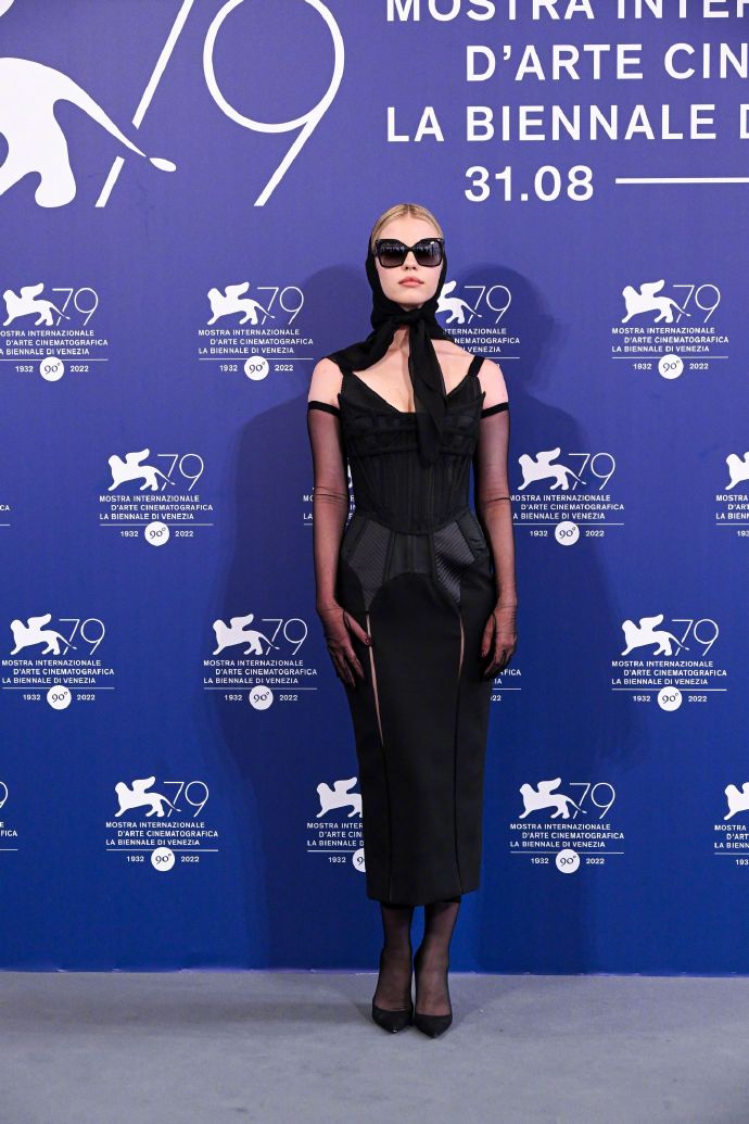 Mia Goth is wearing a black gown, paired with black gloves, a black headscarf, and black sunglasses.