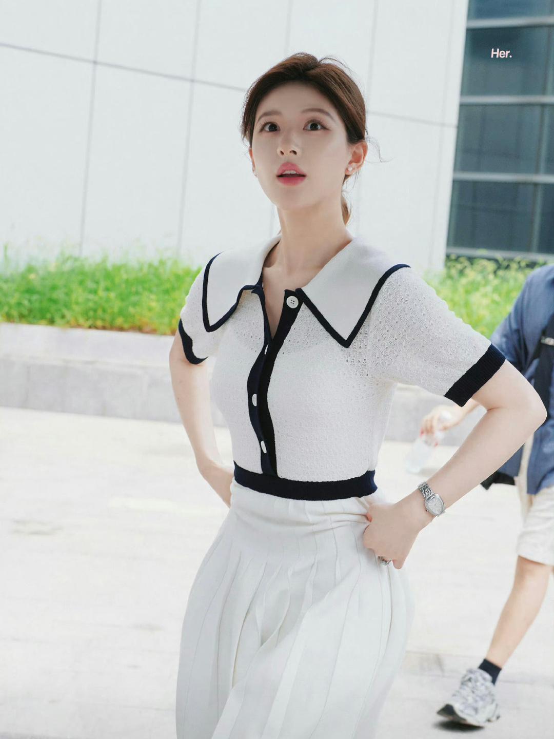 A girl wearing a white knit top and a white pleated skirt.