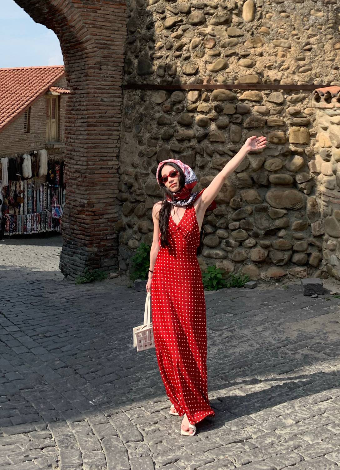 A young lady is taking photos at a tourist spot in a red and white polka dot maxi dress