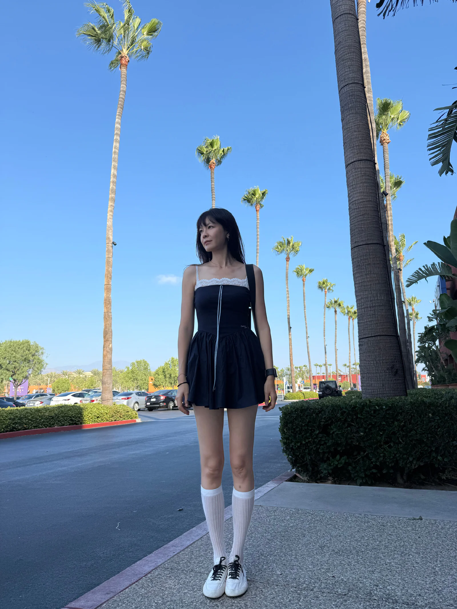 Chic Black Mini Dress with Lace Detail, White Knee-High Socks, and Sneakers