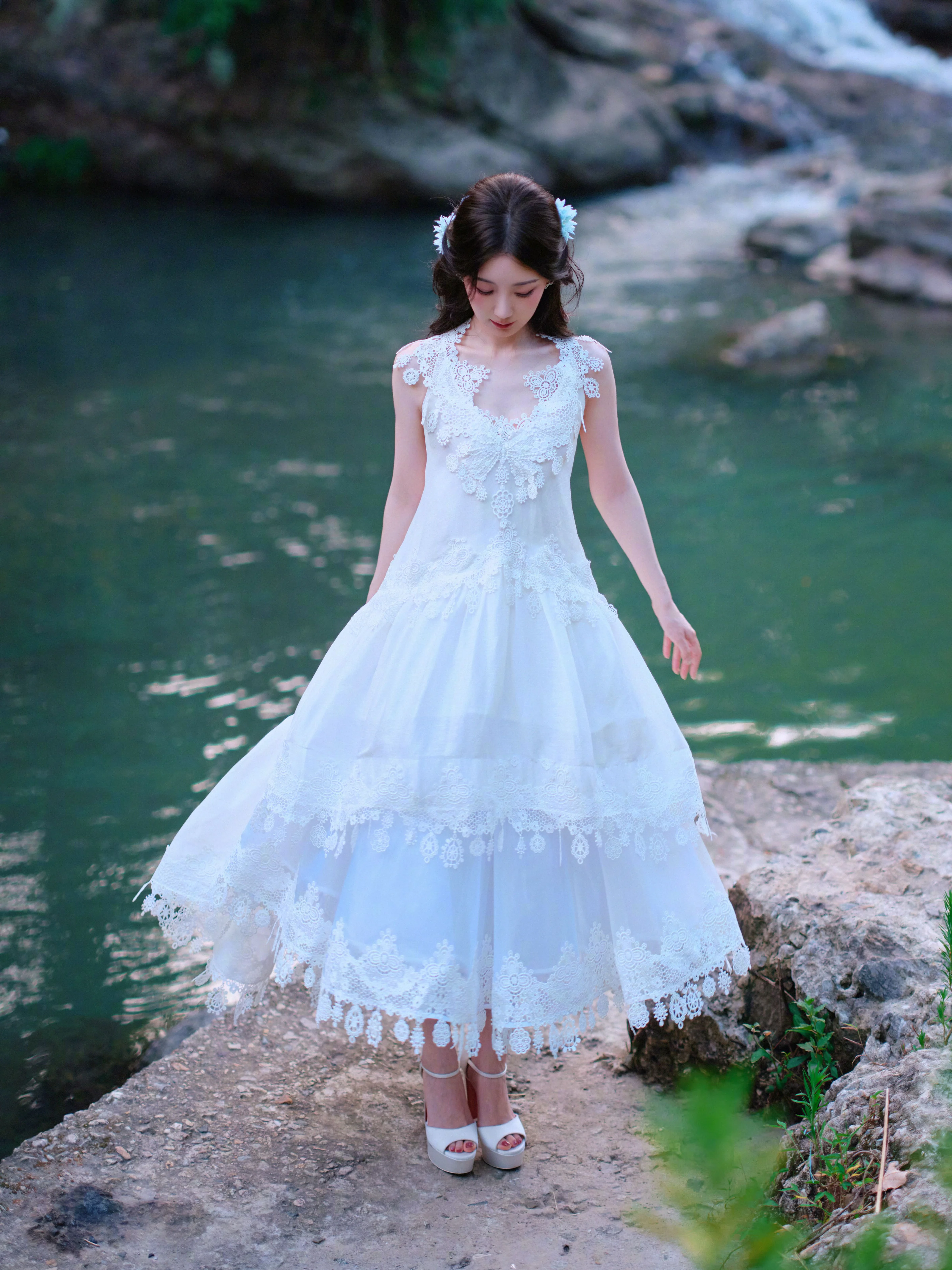 Elegant White Lace Dress with Layered Skirt and Floral Accents by the Water