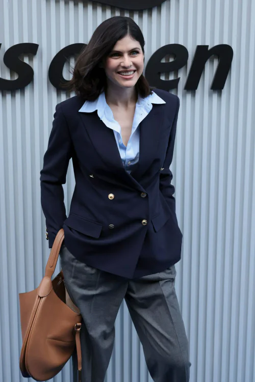 Alexandra Daddario's outfit for the US Open 2025. Navy Blazer and Gray Trousers Ensemble with Light Blue Shirt and Tan Handbag