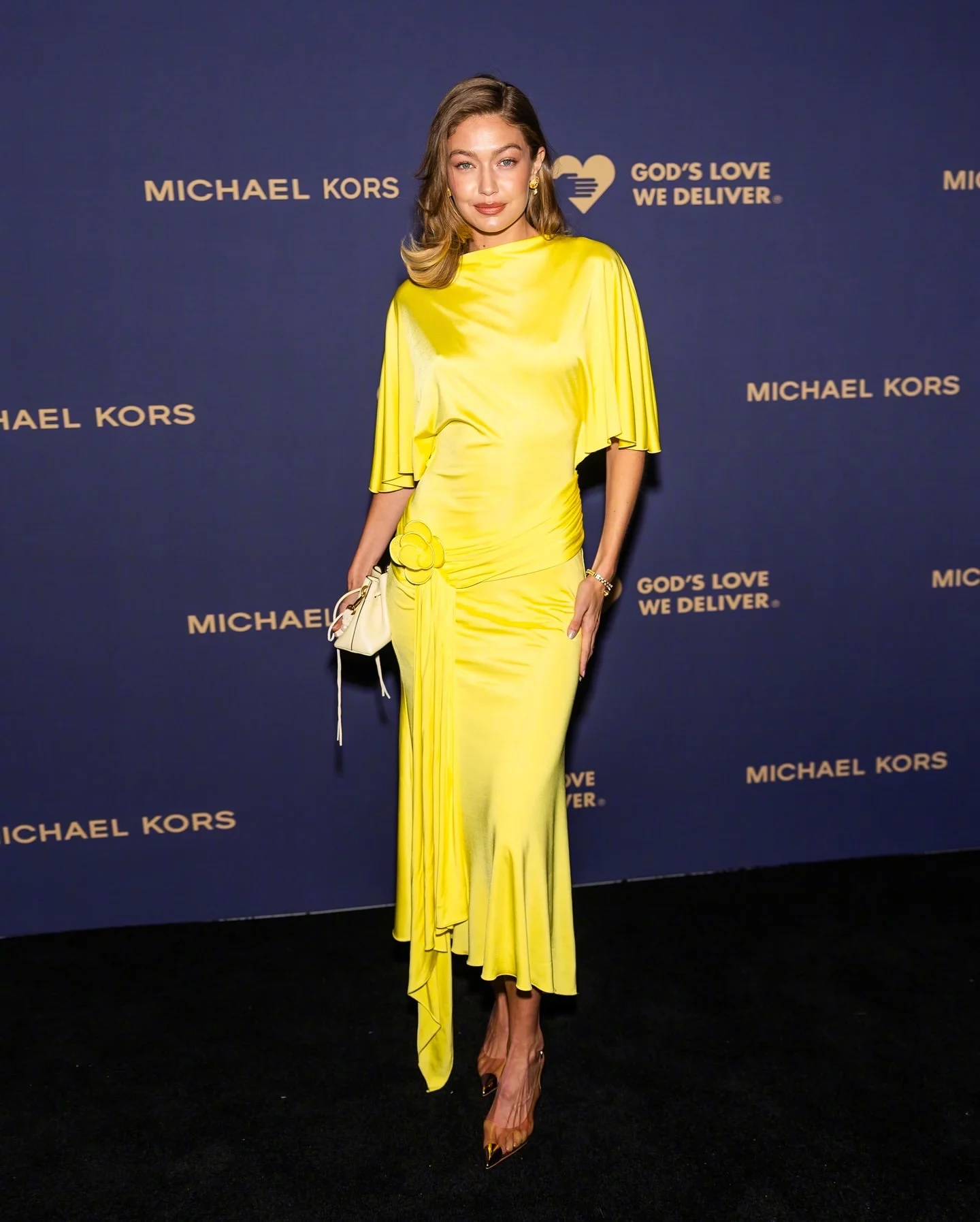 Gigi Wore a Vibrant Yellow Satin Dress with Asymmetrical Hem and Floral Detail